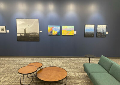 interior photo of a blue wall with five artworks hanging on it in front of a low table and couch