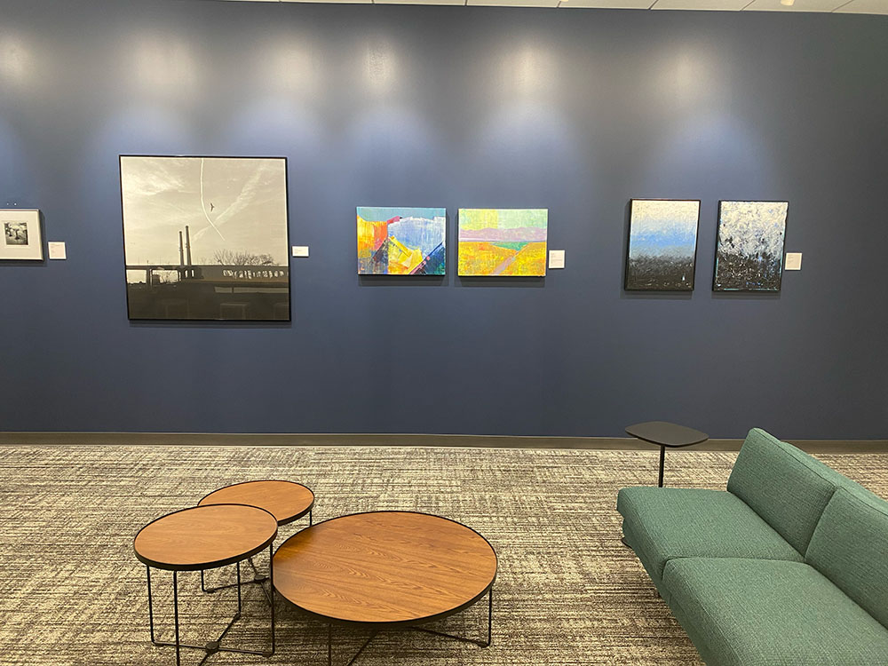 interior photo of a blue wall with five artworks hanging on it in front of a low table and couch